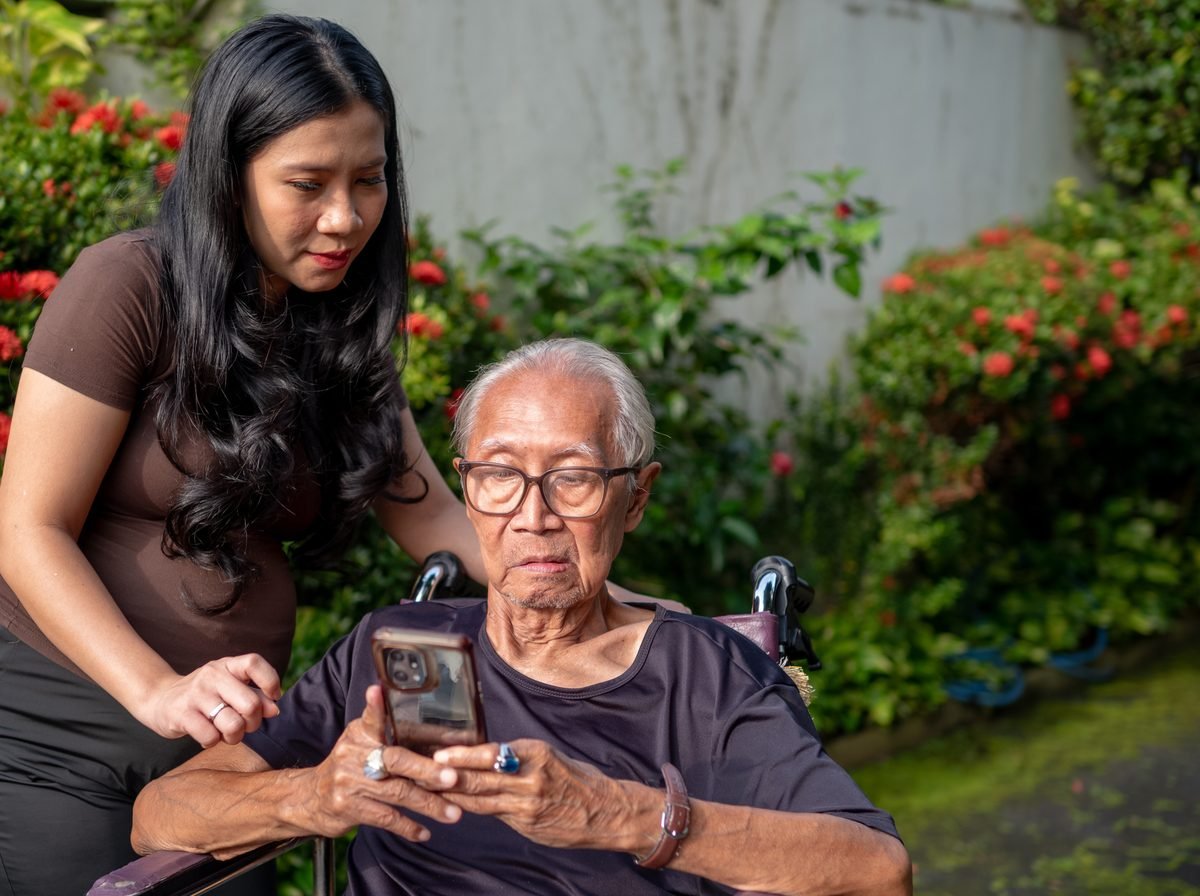 A family caregiver helping an older patient look at a phone together outdoors